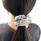Person with a gray scrunchie with silver chain detail in a ponytail on a white background